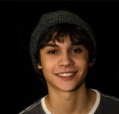 a young man wearing a knitted hat and smiling at the camera with a black background