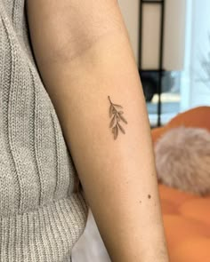 a woman's arm with a small leaf tattoo on the left side of her arm