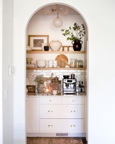 an archway leads into a kitchen with white cabinets and open shelving, filled with pots and pans