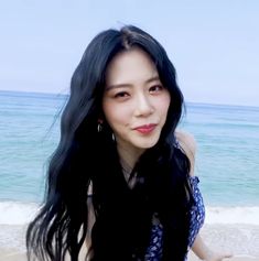 a woman with long black hair standing on the beach