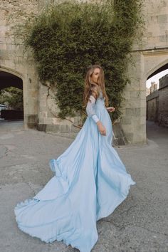 a woman wearing a blue dress standing in front of a stone wall