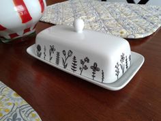 a white cake dish sitting on top of a wooden table next to a red and white vase