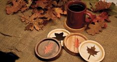 four wooden coasters with maple leaves and a coffee mug on the table next to them