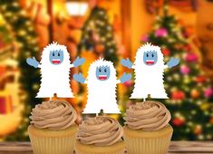 three cupcakes with frosting in front of a christmas tree