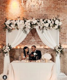 a bride and groom sitting at a table in front of a chandelier with white flowers