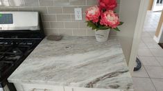 some pink flowers are in a white vase on a marble counter top next to a stove