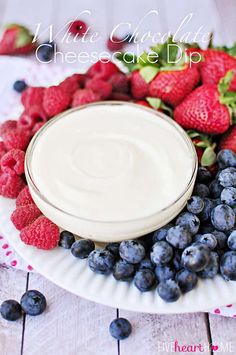 a white chocolate cheesecake dip surrounded by blueberries and strawberries on a paper plate