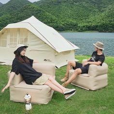 two people sitting on chairs in front of a lake with a tent and mountains in the background