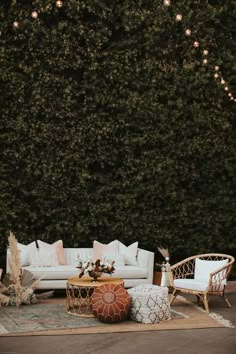 an outdoor seating area with white couches, pillows and lights hanging from the trees