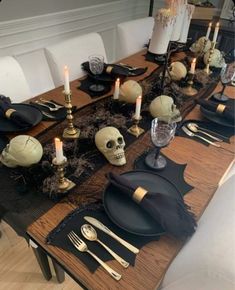 the table is set with black and gold plates, silverware, candles and skulls