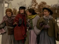 four women are standing together outside in the snow wearing dresses and hats with fur stolers