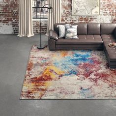 a living room with a sectional couch and colorful rugs on the floor in front of a brick wall