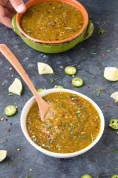 a hand holding a wooden spoon over a bowl filled with green soup and garnished with chopped jalapenos