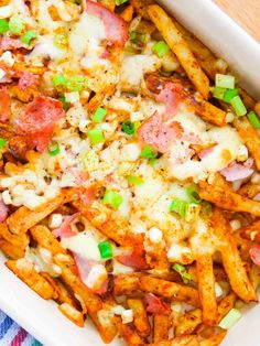 a white casserole dish filled with pasta, ham and cheese covered in green onions