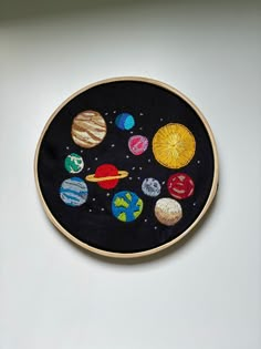 an embroidered wall hanging on the side of a white wall with space and planets painted on it