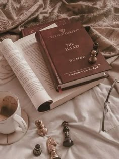 an open book sitting on top of a bed next to a cup of coffee and eyeglasses