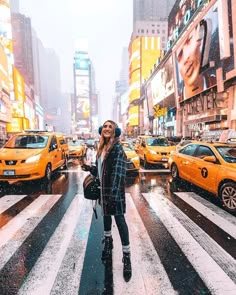 a woman standing in the middle of a crosswalk on a snowy day with taxis