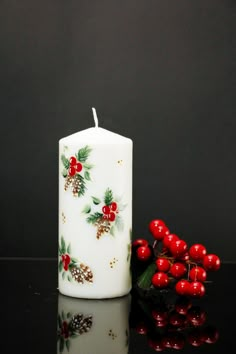 a white candle with holly and berries on it next to some red berries, which are still in the foreground