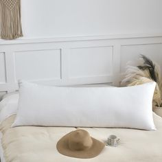 a white pillow with a brown hat on top of it next to a small feather