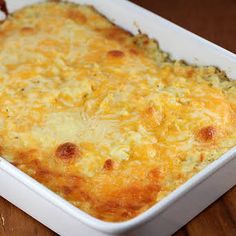 a casserole dish with cheese on top sitting on a wooden table next to a fork