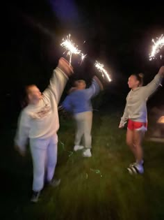 three people are holding sparklers in the air while standing on some grass at night