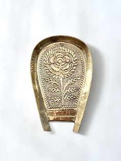 a gold plate with a flower design on the front and back of it, sitting on a white surface