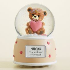 a teddy bear holding a heart in a snow globe