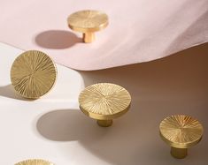 three gold knobs on a white surface with pink sheets in the backround