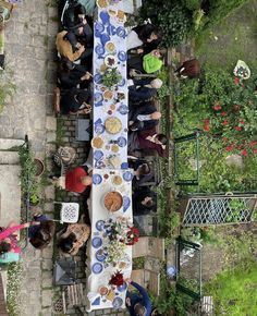 an overhead view of a long table with people sitting at it in the middle of a garden