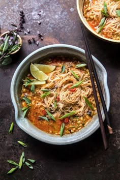 two bowls filled with noodles and vegetables next to chopsticks on a table top