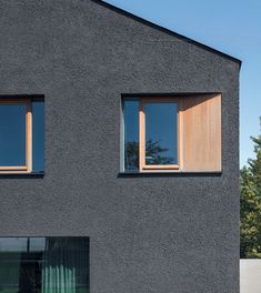 two windows on the side of a gray building with trees in the backround