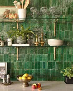 a kitchen with green tiles on the wall and shelves above it is filled with fruit