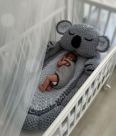 a baby sleeping in a crib with a stuffed koala bear