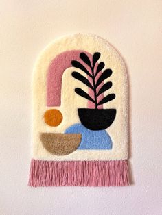 a wall hanging with a plant and bowl on it