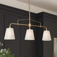 three lights hanging from the ceiling in a room with dark wood cabinets and white flowers