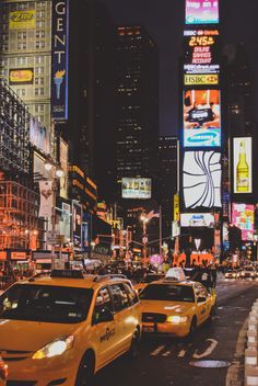 taxi cabs and taxis driving down a busy city street at night with billboards in the background