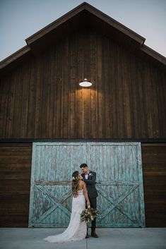 a bride and groom standing in front of a barn door at their wedding day with the sun shining on them