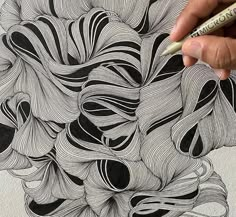 a person is drawing something with black and white lines on the paper while holding a marker