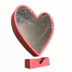 a heart shaped mirror sitting on top of a pink stand next to a white wall