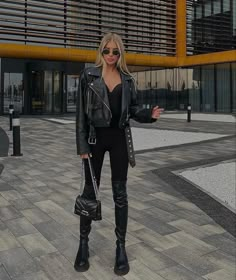 a woman in black outfit and boots standing on the street with her hand out to someone