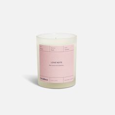 a white candle with pink labels on the top and bottom, in front of a white background