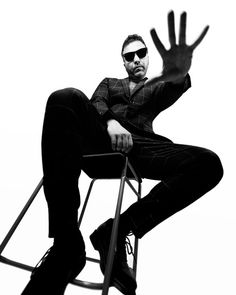 a man sitting on top of a chair with his hand up in the air while wearing sunglasses