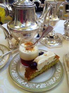 a piece of cake on a plate next to a silver tea pot and two cups