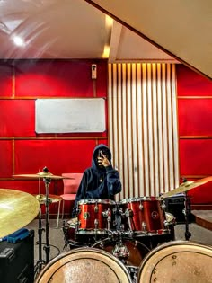 a man sitting in front of a drum set talking on a cell phone while wearing a hoodie