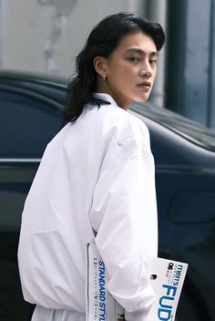 a woman walking down the street with a book in her hand while wearing a white coat