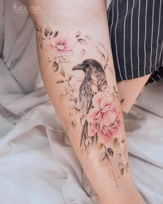 a woman's leg with flowers and a bird on it, sitting on a bed