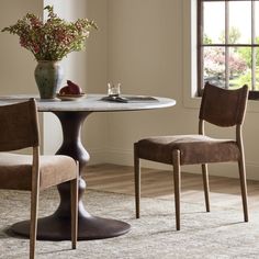 a dining room table with two chairs and a vase full of flowers on the table