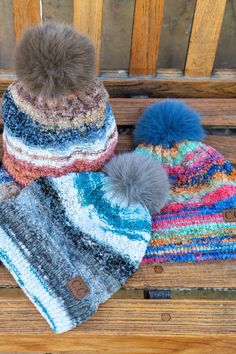 three hats sitting on top of a wooden bench next to each other and one has a pom - pom