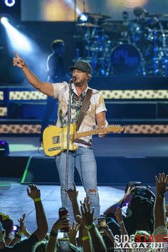 the singer is holding his guitar and singing to an audience at a concert with their hands in the air