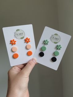 two pairs of earrings are being held up in front of the camera, one has an earring with flowers on it